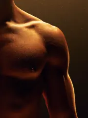 A lean, muscular chest and shoulder lit in warm gold